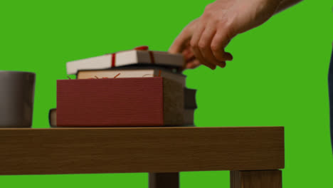 Close-Up-Of-Man-Opening-Gift-Wrapped-Present-On-Table-Shot-Against-Green-Screen